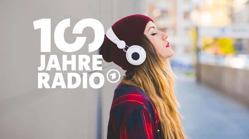 Eine Frau trägt Kopfhörer und hat die Augen geschlossen, daneben steht "100 Jahre Radio" in weißer Schrift.