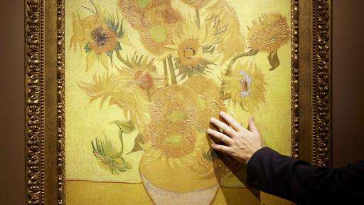 Eine Hand greift nach einer Reproduktion des Bildes "Sonnenblumen" des Malers Vincent van Gogh