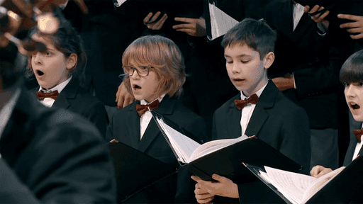 Kinder in Anzügen singen mit Kladden in den Händen.