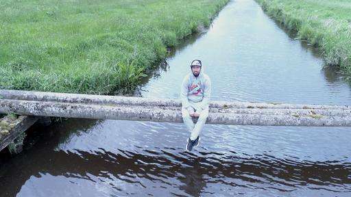 Ein Mann mit Kapuzenpulli sitzt auf Betonrohren über einem Fluss