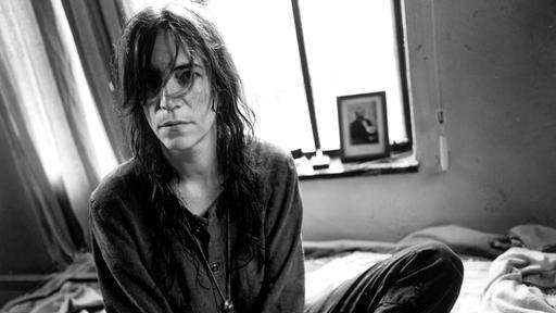 Patti Smith sitzt auf einem Bett.