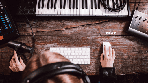 Eine Person an einem Arbeitsplatz mit Computer, Keyboard, Mischpult und Mikrofon.