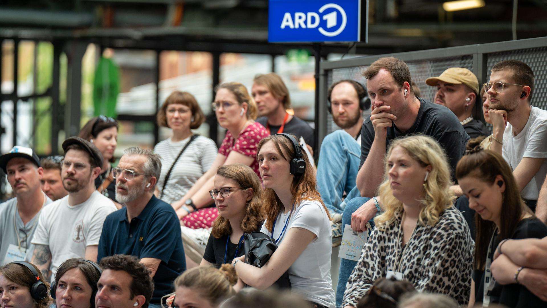 Publikum sitzt auf einer Tribüne.