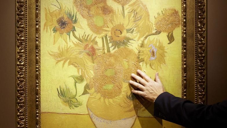 Eine Hand greift nach einer Reproduktion des Bildes "Sonnenblumen" des Malers Vincent van Gogh