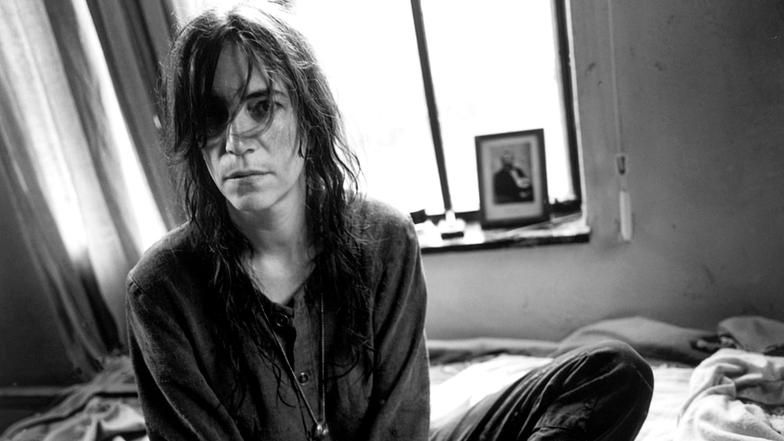 Patti Smith sitzt auf einem Bett.