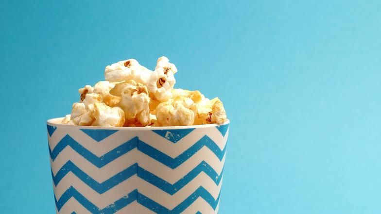 Ein Becher mit Popcorn auf blauem Hintergrund.