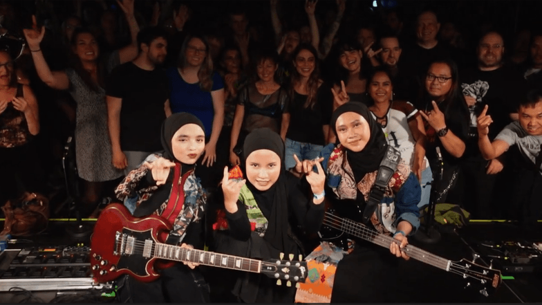 Drei Frauen mit E-Gitarren und in Hijab gekleidet auf einer Bühne.