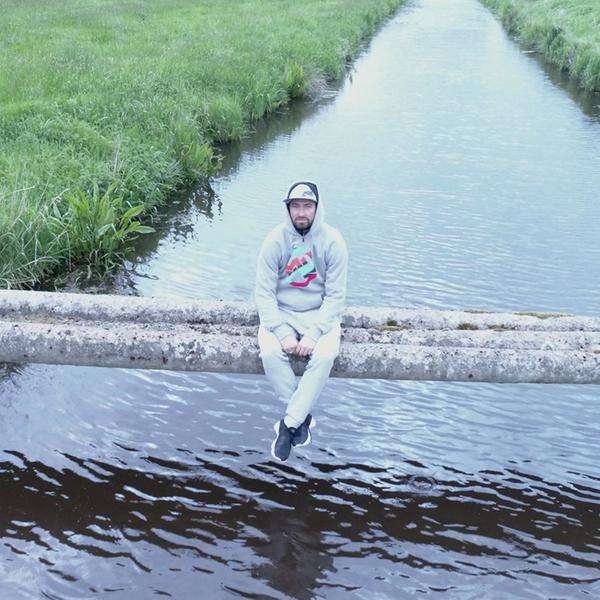 Ein Mann mit Kapuzenpulli sitzt auf Betonrohren über einem Fluss