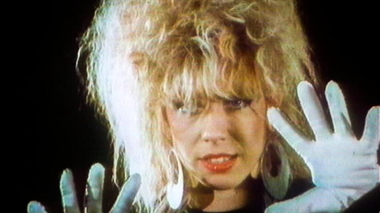 Still eines 80er-Jahre Musikvideos mit einer Frau mit Handschuhen, die in die Kamera gestikuliert