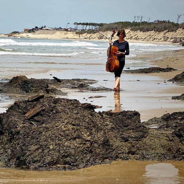 Eine Frau trägt ein Cello über einen Strand
